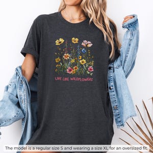 Puede incluir: Camiseta de color gris oscuro jaspeado con un dise&ntilde;o floral y el texto "LIVE LIKE WILDFLOWERS".