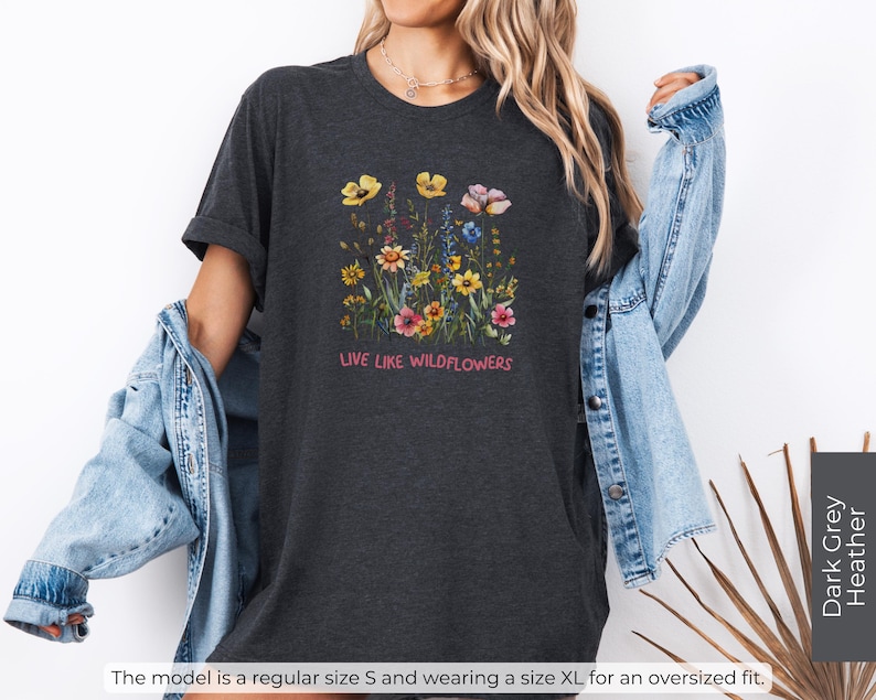Puede incluir: Camiseta de color gris oscuro jaspeado con un dise&ntilde;o floral y el texto "LIVE LIKE WILDFLOWERS".