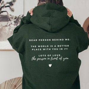Pu&ograve; includere: Felpa con cappuccio verde scuro con testo bianco che dice "Cara persona dietro di me: Il mondo &egrave; un posto migliore con te dentro! Tanto amore, la persona davanti a te".
