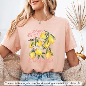 K&ouml;nnte beinhalten: Ein pfirsichfarbenes T-Shirt mit einem Zitronenmotiv und dem Text "squeeze out kindness".