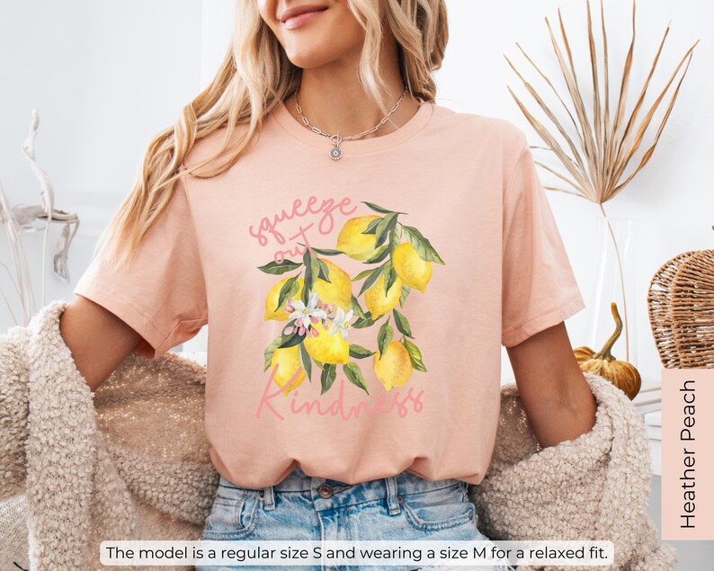 K&ouml;nnte beinhalten: Ein pfirsichfarbenes T-Shirt mit einem Zitronenmotiv und dem Text "squeeze out kindness".