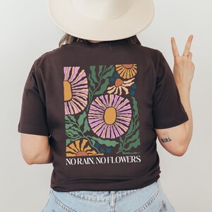 May include: A brown t-shirt with a floral design and the text "NO RAIN, NO FLOWERS".