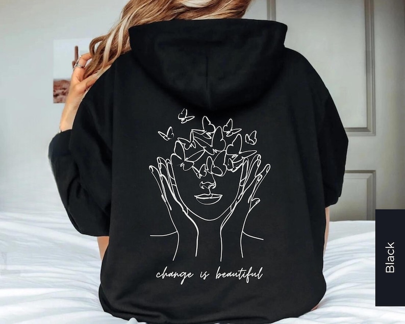 May include: Black hooded sweatshirt with a white graphic of a face with butterflies around it. The text "change is beautiful" is printed below the graphic.