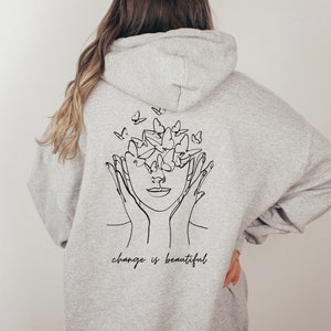 May include: Gray hooded sweatshirt with a black line drawing of a face with butterflies around it. The text "change is beautiful" is printed below the drawing.
