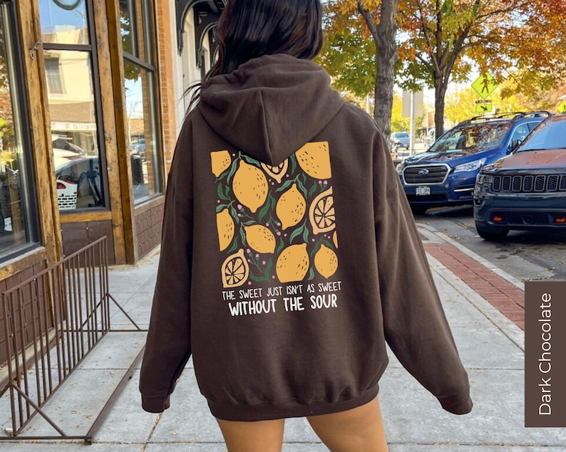 K&ouml;nnte beinhalten: Ein brauner Hoodie mit einem Zitronendruck und dem Text "The sweet just isn't as sweet without the sour" auf der R&uuml;ckseite. Dunkle Schokolade.