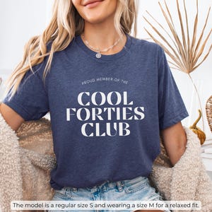 May include: A navy blue t-shirt with the text "Proud Member of the Cool Forties Club" in white lettering.
