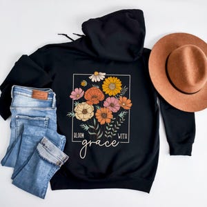 May include: Black hooded sweatshirt with a floral design and the text "Bloom with grace".