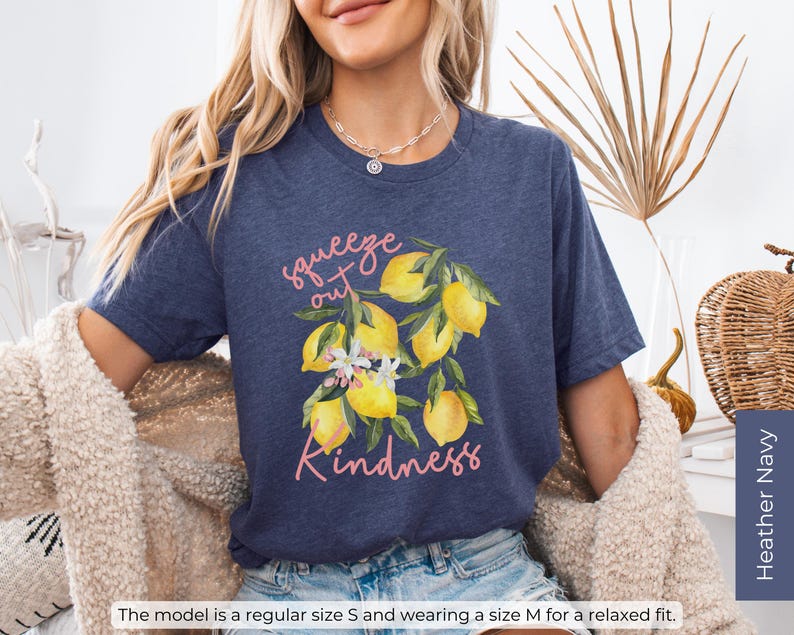 K&ouml;nnte beinhalten: Ein marineblaues T-Shirt mit einem Motiv aus Zitronen und Blumen. Der Text "squeeze out kindness" ist in Pink auf dem Shirt gedruckt.