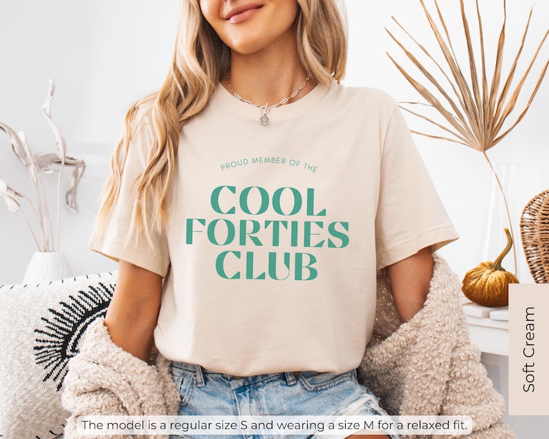 May include: A beige t-shirt with the text "PROUD MEMBER OF THE COOL FORTIES CLUB" in green lettering.
