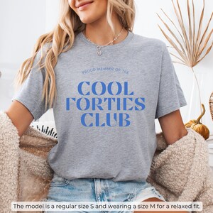 May include: Gray t-shirt with the text "PROUD MEMBER OF THE COOL FORTIES CLUB" in blue letters.