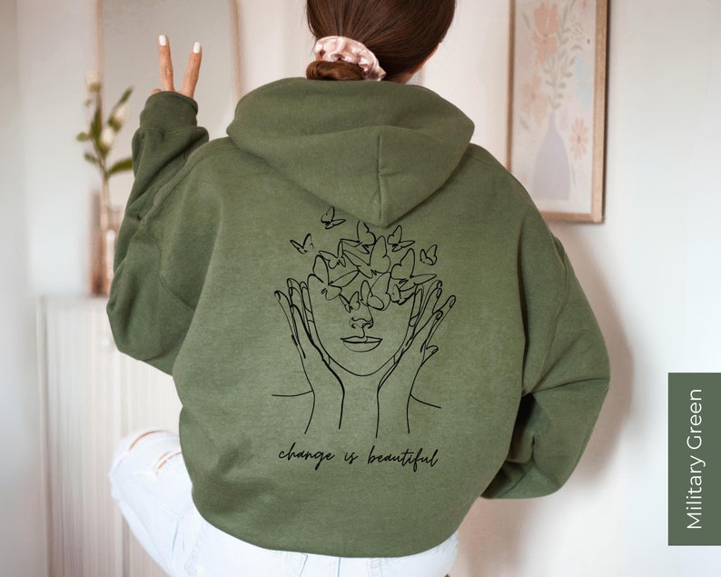 May include: A green hooded sweatshirt with a black line drawing of a face with butterflies around it. The text "change is beautiful" is printed below the drawing.