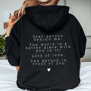 May include: Black hoodie with a white message on the back that reads "Dear person behind me: The world is a better place with you in it! Lots of love, The person in front of you".