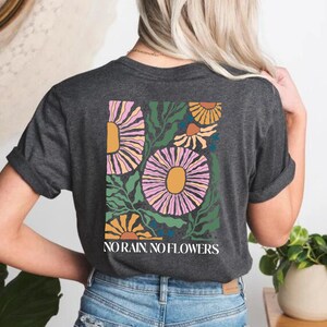 May include: A dark grey heather t-shirt with a floral design and the text "NO RAIN. NO FLOWERS." printed on the back.
