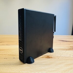 Könnte beinhalten: Ein schwarzer Dell Desktop-Computer mit einem schwarzen Ständer. Der Computer hat ein Dell-Logo und verschiedene Anschlüsse auf der Vorderseite. Der Computer steht auf einer Holzoberfläche.