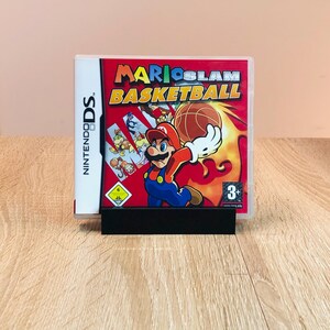Könnte beinhalten: Eine Nintendo DS-Spielebox für Mario Slam Basketball. Die Box ist rot und zeigt ein Cartoon-Bild von Mario beim Basketballspielen. Das Spiel ist für 3+ Jahre geeignet.