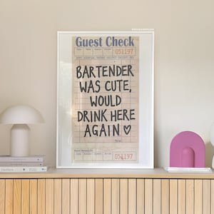 May include: A framed print of a vintage guest check with the handwritten message "Bartender was cute, would drink here again". The check is dated 051197.