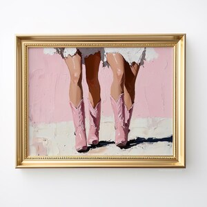 May include: A painting of two pairs of legs wearing pink cowboy boots against a pink background. The painting is framed in a gold frame.