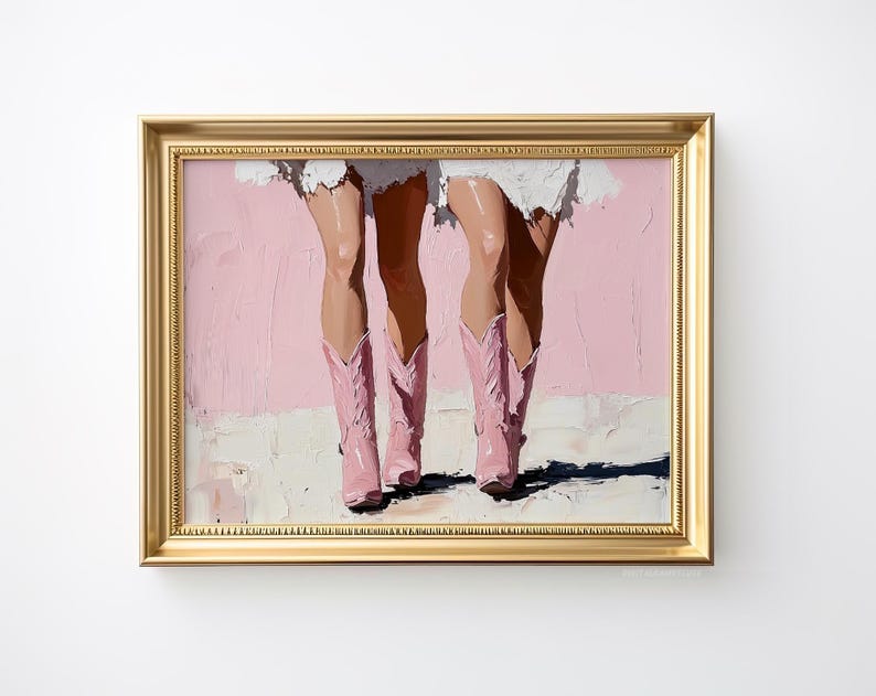 May include: A painting of two pairs of legs wearing pink cowboy boots against a pink background. The painting is framed in a gold frame.