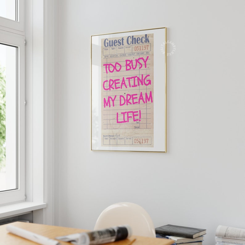 May include: A framed print of a guest check with the text "Too Busy Creating My Dream Life!" written in pink on a white background.