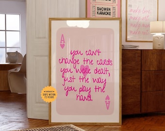 Puede incluir: Un estampado artístico rosa enmarcado con el texto "you can't change the cards you were dealt, just the way you play the hand." El estampado presenta un diseño de carta de As de corazones. Se ven otros estampados enmarcados.