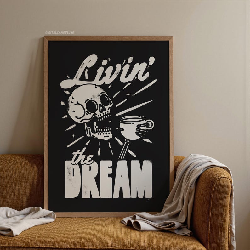 May include: Black framed art print with a skull holding a coffee cup, with the words "Livin' the Dream" in white. The art is displayed on a mustard-colored couch with a beige blanket.