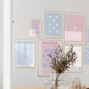May include: A wall gallery featuring eight framed prints with a pink and blue color scheme. The prints include text such as "Good Times", "You Look So Good", and "What A Time To Be Alive".  There are also two playing card prints, one with an eight of hearts and the other with an ace of hearts.