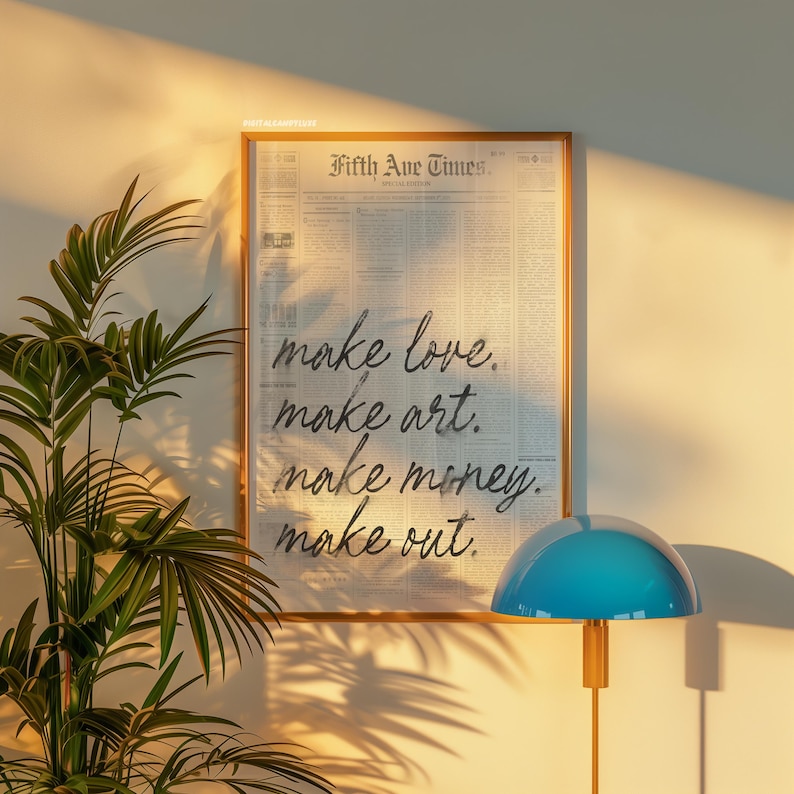 May include: A framed print with the text "Fifth Ave Times." and the words "make love. make art. make money. make out." in a handwritten style. The frame is a light brown color, and the background is a newspaper print.