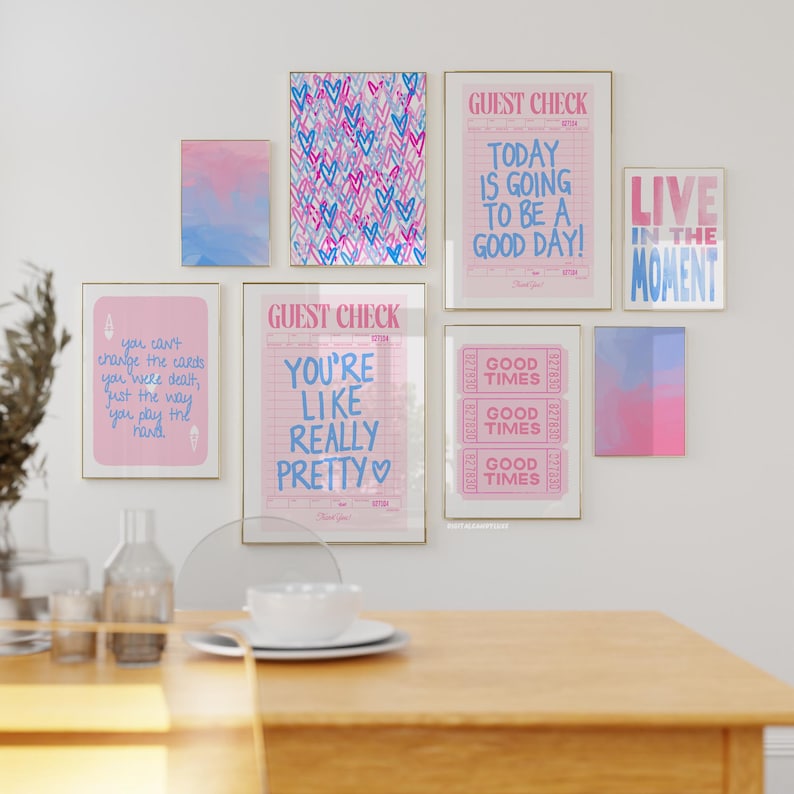 May include: A collection of eight framed prints with pink and blue color schemes. The prints feature various motivational quotes and designs, including hearts, a guest check, and a ticket stub. The prints are arranged on a white wall above a wooden table.