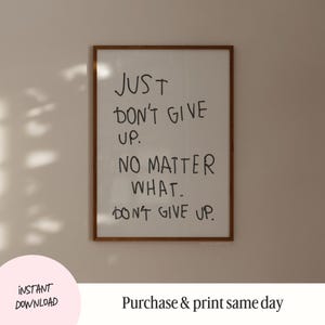 May include: A framed print with the text "JUST DON'T GIVE UP. NO MATTER WHAT. DON'T GIVE UP." in black handwritten font on a white background.