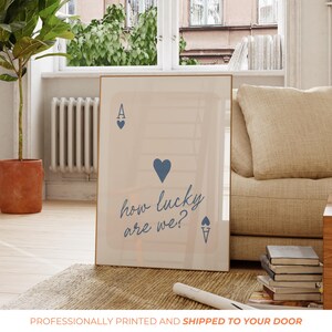 Pu&ograve; includere: Un poster beige con un design di carta da gioco di asso di cuori blu. La carta ha un cuore blu al centro e il testo "how lucky are we?" scritto in corsivo.