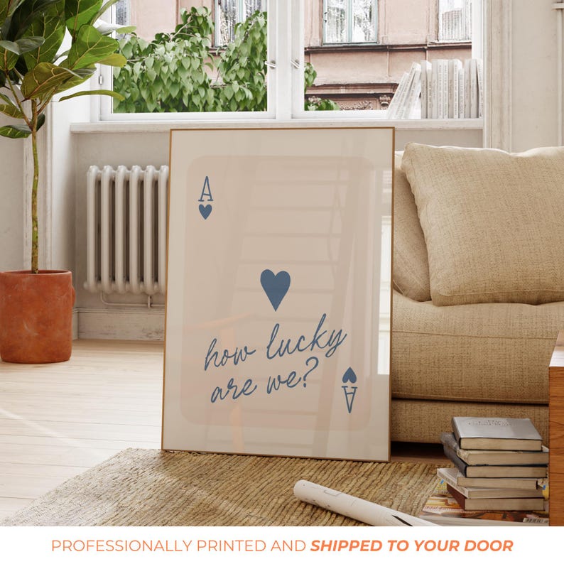 Pu&ograve; includere: Un poster beige con un design di carta da gioco di asso di cuori blu. La carta ha un cuore blu al centro e il testo "how lucky are we?" scritto in corsivo.