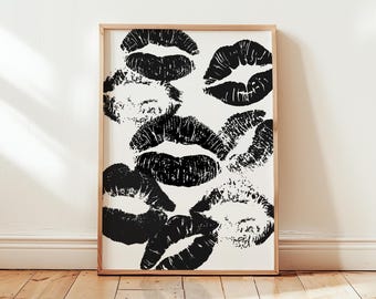 Puede incluir: Impresión enmarcada con múltiples marcas de besos de lápiz labial negro sobre un fondo blanco. La obra de arte se muestra en un marco de madera marrón claro. La impresión está contra una pared blanca, con un suelo de madera en primer plano.