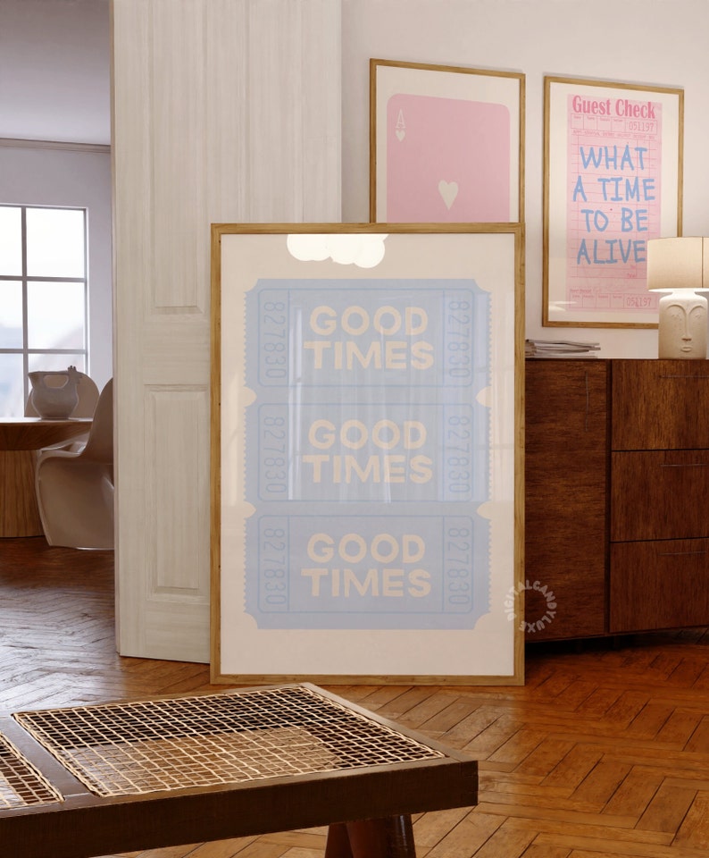 May include: A framed print with a light blue background and white text that reads "Good Times" repeated three times. The print is in a wooden frame and is hanging on a wall in a room with a wooden floor.