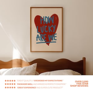 May include: A framed art print featuring a large red heart with the words "HOW LUCKY ARE WE" in blue. The artwork is displayed above a wooden headboard. The print has a cream-colored background and a wooden frame.