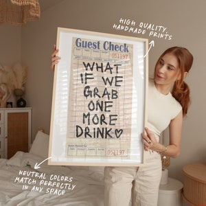 May include: A framed print of a vintage guest check with the handwritten text "What if we grab one more drink" and a heart. The print is in a light wood frame and has a neutral colour palette.