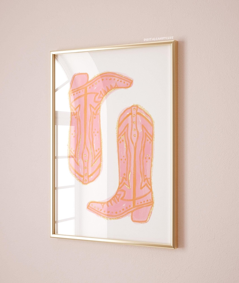 Puede incluir: Una impresi&oacute;n enmarcada de dos botas de vaquero rosas con detalles dorados. Las botas est&aacute;n dibujadas de forma sencilla y estilizada.