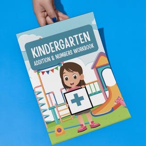 Può includere: Un quaderno di lavoro intitolato "KINDERGARTEN ADDITION & NUMBERS WORKBOOK" è tenuto su uno sfondo blu. La copertina presenta un'illustrazione a cartoni animati di una ragazza che tiene in mano un cartello con un simbolo più, con un parco giochi sullo sfondo.