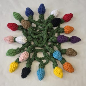May include: A crocheted Christmas light display featuring a variety of colorful bulbs, including red, blue, yellow, and white. The bulbs are connected by a green crocheted cord, creating a festive and handmade decoration. The lights are arranged in a circular pattern.