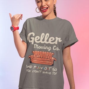 Könnte beinhalten: Graues T-Shirt mit dem Text "Geller Moving Co." und einem Cartoon-Bild eines orangefarbenen Sofas. Unter dem Sofa steht der Text "WE P.I.V.O.T SO YOU DON'T HAVE TO!"