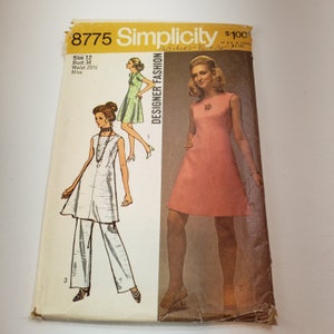 Op de afbeelding: Vintage Simplicity Designer Fashion naaipatroon, maat 12, met illustraties van jurken en een broekpak. De omslag toont een vrouw in een roze jurk en andere ontwerpen in groen en wit. Het patroon komt uit de jaren 1960 of 1970.