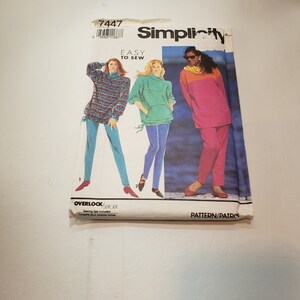 May include: Simplicity sewing pattern number 7447, easy to sew, with three different outfit options. The first outfit is a colorful sweater with blue pants. The second outfit is a green sweater with blue pants. The third outfit is a pink top with pink pants.
