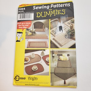 Op de afbeelding: Een Simplicity naaipatroon voor placemats en tafellopers. Het patroon bevat verschillende placemat-ontwerpen, waaronder rechthoekige en ovale vormen. De omslag bevat de tekst "Sewing Patterns for Dummies" en illustraties van de afgewerkte producten.