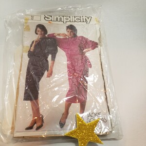 May include: A Simplicity sewing pattern for a dress, featuring two models wearing the dress in black and pink. The pattern is labeled "Simplicity" and "Jackie Rogers".