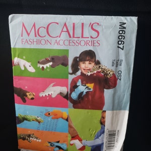 May include: A McCall's sewing pattern for making finger puppets. The pattern includes instructions for making a variety of animal puppets, including a wolf, a shark, a crocodile, a monkey, a giraffe, and a leopard. The pattern is for size OSZ. The pattern number is M6667.