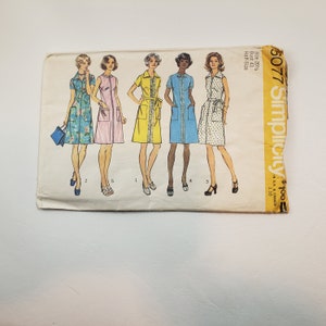 May include: A vintage Simplicity sewing pattern for five different dresses. The pattern is for sizes 20 1/2 to 22 1/2, bust 43, half size. The pattern is for a dress with a button-up front, short sleeves, and a skirt that falls to the knee. The pattern is printed on a white background with black and yellow text.