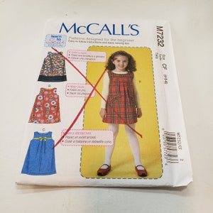 May include: McCall's sewing pattern M7232 for girls' dresses. The pattern features illustrations of three dress designs, including a red plaid jumper dress. The package includes instructions for beginners, with the text "Learn to Sew for Fun."