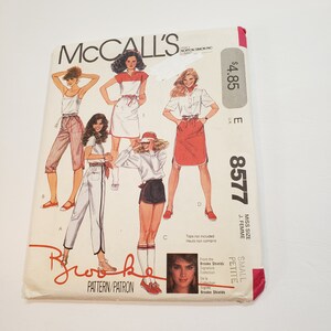 May include: McCall's sewing pattern number 8577 for a small petite miss size, featuring a Brooke Shields Signature Collection design. The pattern includes four different styles of clothing: a white tank top with red shorts, a white shirt with a red skirt, a white shirt with a red and white striped skirt, and a white shirt with a red and white striped skirt. The pattern is priced at £3.90.
