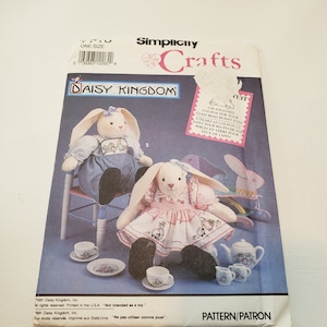 May include: A Simplicity Crafts pattern for making two plush bunny dolls. The pattern includes instructions for making a tea set with a teapot, cups, and saucers. The pattern is titled "Daisy Kingdom" and includes a coupon for glass bead bunny eyes.