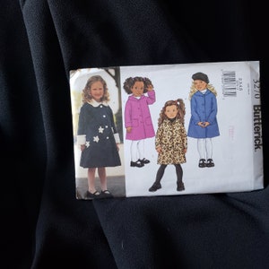 Op de afbeelding: Een naaipatroon voor vier verschillende kinderjassen. Het patroon bevat een zwarte jas met witte sterren, een roze jas, een blauwe jas en een jas met luipaardprint. Het patroon is van Butterick en is maat 32/70.