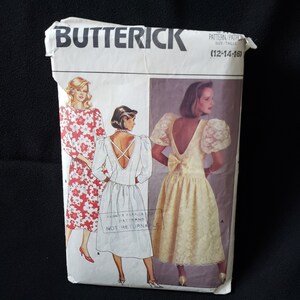 May include: A vintage sewing pattern for a dress with a low back and a bow. The pattern is for sizes 12-14-16. The pattern is from Butterick.